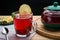 Berry tea in a cup next to a teapot spoon and lemon and lemon balm and jam in a vase on a round stand and a napkin.