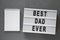 `Best dad ever` words on lightbox, blank notepad over gray background, top view. Overhead, from above, flat lay