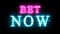 Bet Now glowing neon inscription on brick wall background.