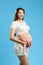 Beuatiful smiling pregnant woman in white T-shirt and shorts with pink ribbon on her belly