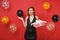 Bewildered irritated girl in black dress spreading hands, holding red box with gift, present on bright red background