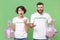 Bewildered irritated two young friends couple in white volunteer t-shirt isolated on pastel green wall background