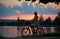 Bewitching sunset landscape. Silhouette of woman in dress rides a retro bike with basket on road near the river