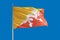 Bhutan national flag waving in the wind on a deep blue sky. High quality fabric. International relations concept