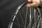 A bicycle mechanic holds a bicycle wheel in his hand on a black background. The rim and the specialist\'s hand are close-up.