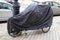 Bicycle protected by dark grey blue protective cover tarpaulin jacket tricycle bike in street