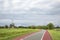 Bicycle road and a mill in Holland with red cycle path on both sides, perspective, under cloudy skies and between green meadows