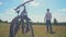 Bicycle Traveler Stands with Arms Outstretched in the Field. In the foreground Bicycle. Sunny Bright Day. Healthy Man