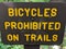 Bicycles prohibited on trails sign, yellow letters on brown sign