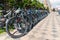 Bicycles stand in a row on a cobbled sidewalk in a residential area