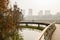 Bicyclist on curving footbridge over river near city in sunny