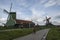 Bicyclists ride down a path past traditional windmills on a cloudy day at Volendam, located on the Markermeer Lake, northeast of