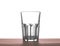 A big beautiful empty glass for water, juice or milk on a dark brown wooden table, isolated on a white background.