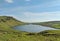 A big beautiful Lake on a mountain surrounded by green hills and cliffs under the bright blue sky.