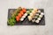 Big beautiful set of different types of sushi maki on a black rectangular stone slate plate.