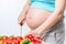 Big belly of pregnant woman in focus, woman preparing salad