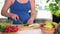 Big belly of pregnant woman and hands cutting cucumber on kitchen table