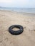 Big black car tire lies on a sandy sea beach