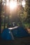 Big blue tent with vestibule. Warm sun rays. Tourist camp among tall pines. Camping in the wilderness. Vertical photo