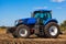 Big blue tractor plows the field and removes the remains of previously mown sunflower.