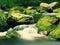 Big boulders covered by fresh green moss in foamy water of mountain river. Light blurred cold water with reflections, white