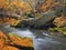 Big boulders with fallen leaves. Autumn mountain river banks. Gravel and fresh green mossy boulders on banks with colorful