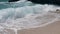 Big breaking waves with sea foams splashing on a white sand beach.