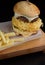 Big burger with egg omelette, cheese and chop alongside french fries on a board