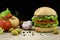 Big buttermilk chiken burger with ingredients on wooden table, dark background.