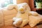 Big children`s toy bear of vanilla color in yellow medical mask sitting sprawled on sofa. Stay at home. Light overlay