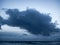 Big, dark, foreboding storm cloud over ocean at dusk.