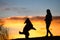 Big dog jumping to take a biscuit from a woman silhouette with background at colorful sunset