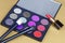 Big eye shadow palette of many colors in lilac, violet and red tones, with two cosmetic brushes and opened red lipstick in luxury