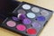 Big eye shadow palette of many colors shades in lilac, violet and red tones, with make up brush of bright lilac powder.