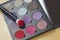 Big eye shadow palette of many colors shades in lilac, violet and red tones, with make up brush of bright red powder.
