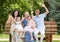 Big family sit on wooden bench in city park and waving, summer season, child, parent and grandmother, group of five people