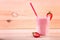 A big glass full of appetizing smoothie. A berry shake on a wooden background. Tasty milkshake with a straw and cut strawberries.