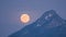 Big golden full moon rising over alpine mountains peak in winter evening