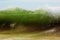 A big green beachbreak wave against blue sky