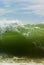 A big green beachbreak wave against sky, vertical orientation