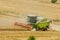 Big green combine harvester machine working in a wheat gold field, mows grass in summer field. Farm machinery harvesting grain in