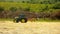 Big green tractor with haymaker working on the meadow in farmland. Haymaking in the countryside below hills