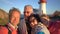 A big happy family takes a selfie or Uses Phone Video Call Camera on the seacoast with an old lighthouse