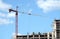Big hoisting tower crane and top section of modern construction building in a city over blue sky with clouds
