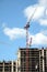 Big hoisting tower cranes and top section of modern construction building in a city over blue sky with clouds