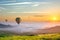 Big hot air baloons over idyllic landscape with green grass covered morning mountains with distant peaks and wide valley full of