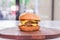 Big juicy double burger on a wooden plate on a table in a restaurant.