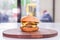 Big juicy double burger on a wooden plate on a table in a restaurant.