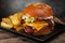 Big juicy hamburger with double cutlet and cheese, french fries in a metal bowl on a wooden table.