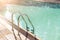 Big luxury empty rectangular swimming pool with clean blue water and ladder at tropical forest beach resort at sunrise morning